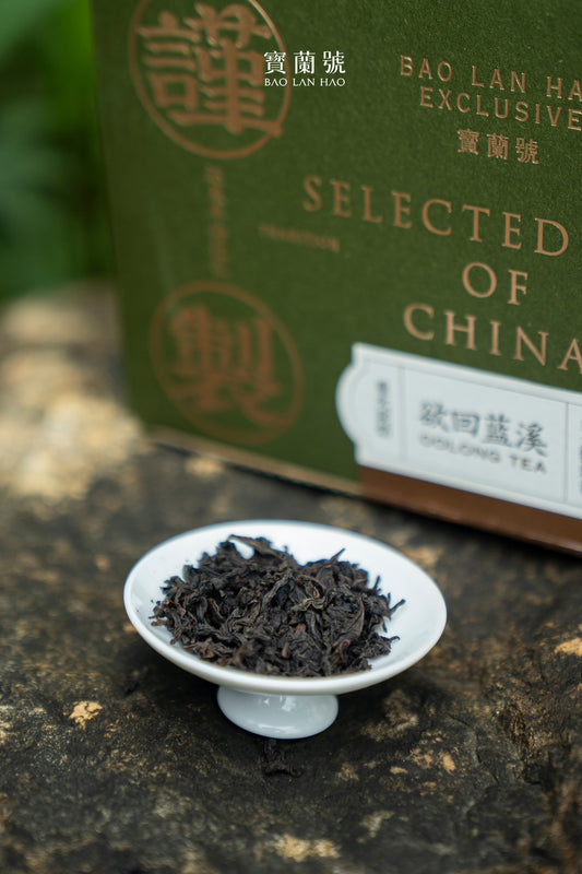 Oolong tea leaves in a white saucer, next to a green tea package