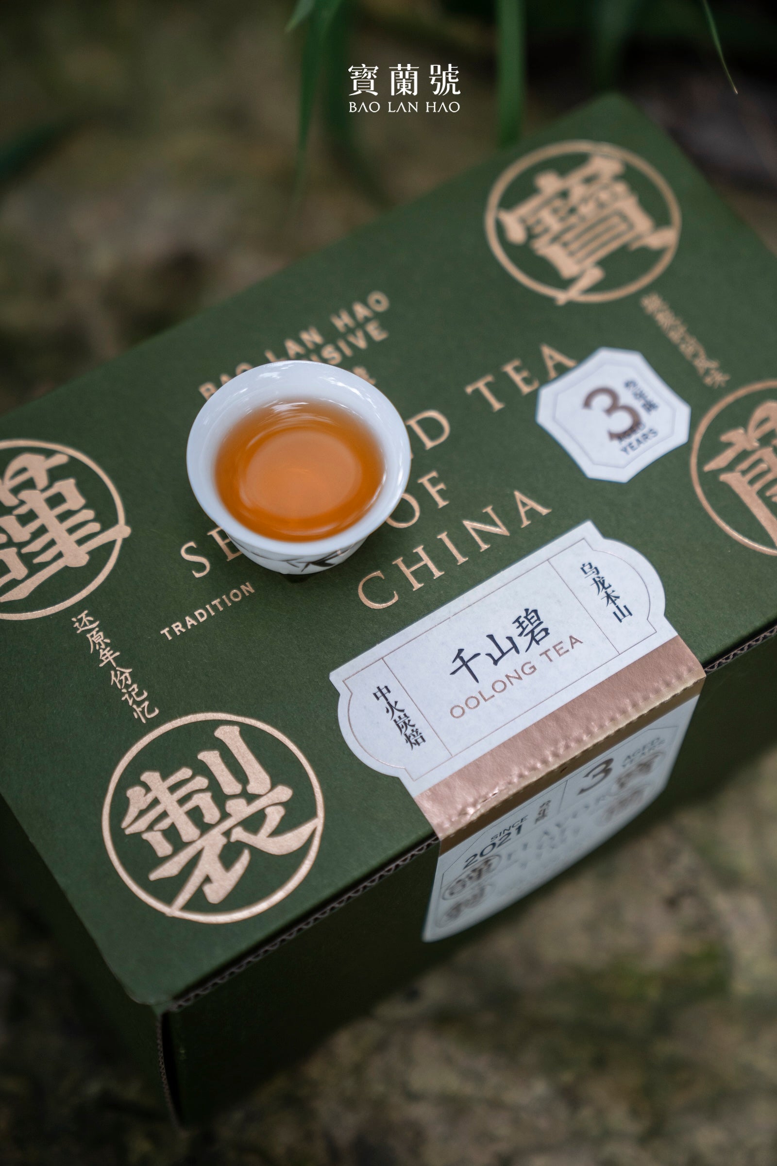 Orange oolong tea in white cup resting on dark green Selected Tea of China tea box