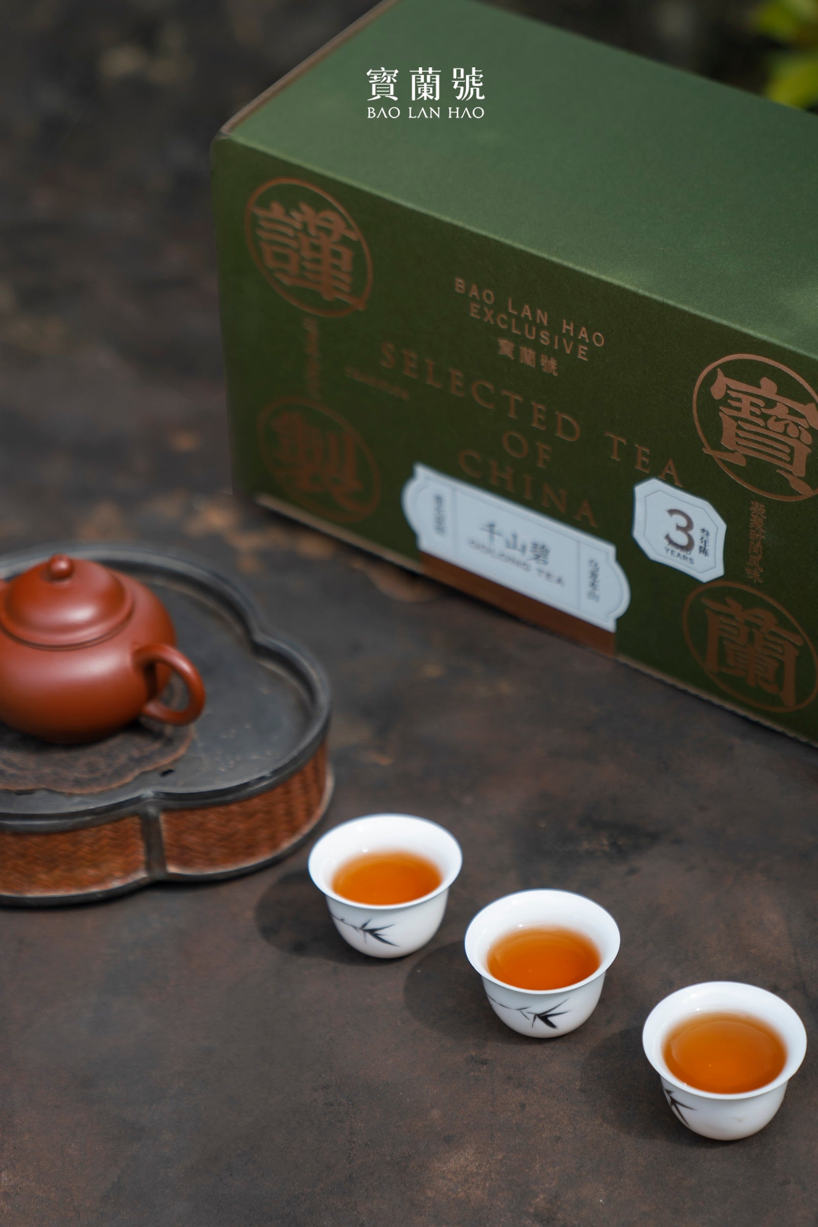 Green tea box with small cups of amber tea and a brown teapot
